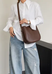 Close-up of dark brown leather bucket bag worn by model in white shirt and jeans.