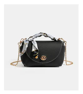 Detail view of black leather bag featuring the turn lock, gold chain and stylish printed scarf.