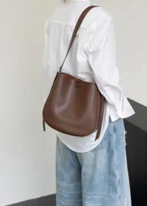 Detail shot showcasing the stylish brown leather bucket bag worn over the shoulder, elegant.