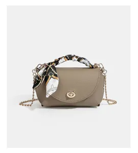 Detail view of taupe leather crossbody bag with chic chain strap and handle silk scarf.
