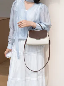 Close-up detail of a chic two-tone leather handbag with a brown flap and cream body, worn by model.