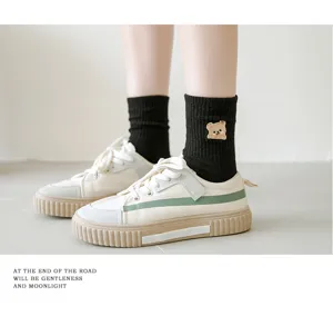 Close-up detail of cute bear embroidered black mid-tube cotton socks paired with shoes.