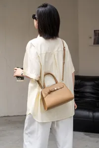 Detail shot of khaki leather shoulder bag with structured handle and metal buckle closure.