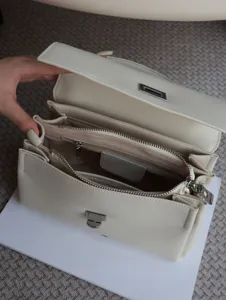 Élégante sac à main en cuir blanc cassé à plusieurs compartiments avec fermoir métallique.