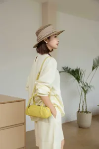 Detailed view of the yellow leather cylindrical handbag styled in a clean lifestyle setting.