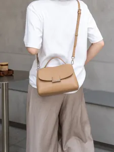 Detail shot of stylish brown leather shoulder bag worn crossbody in a minimalist interior.