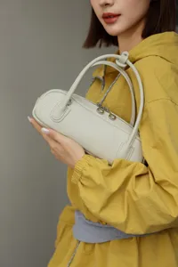 Detailed view of beige leather handbag held by model, showing cylindrical design and texture.
