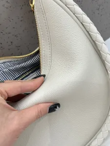 Nahaufnahme einer weißen Leder-Crescent-Hobo-Tasche mit geflochtenem Rand und weicher Textur.
