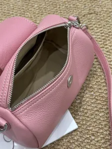 Detailaufnahme einer pinken zylindrischen Schultertasche aus Leder mit glattem Metallreißverschluss.