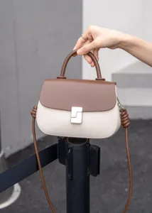 Vista dettagliata di una borsa in pelle bicolore elegante con manico e chiusura in metallo.