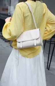 Detail shot of a white leather messenger bag, elegant shoulder strap and flap closure design.