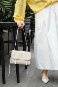 Detailed shot of a minimalist beige leather messenger shoulder bag, casual everyday commute accessory.