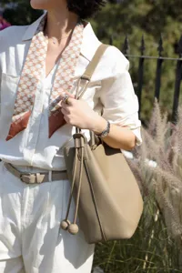 Detail shot of a premium pebbled leather bucket bag styled with a white linen outfit outdoors.