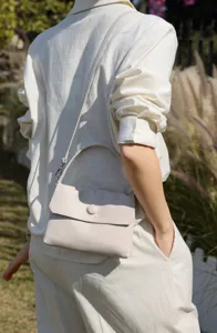 Detail shot of a light beige genuine leather top-handle shoulder bag with button closure.