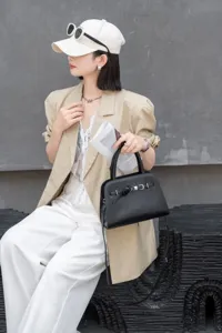 Black leather top handle bag detail showing premium cowhide texture and metal hardware buckle.