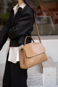Detail shot of the elegant brown leather handbag worn by the model, showcasing texture.