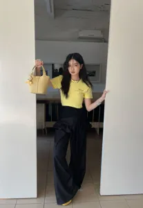 Detailed shot of yellow leather bucket bag with cute bear pendant, worn by model in doorway scene.
