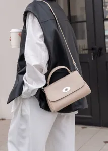 Detailaufnahme einer beige Lederschultertasche mit Metallverschluss im Freien gezeigt.
