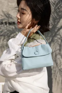 Detail view of a light blue leather handbag with chic button closure and top handle, elegant daily use.