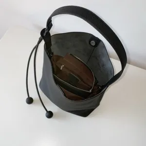 Detailed view of black leather bucket bag, inner zipper pocket, shoulder strap design.