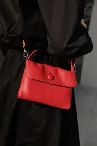 Red genuine leather handbag detail shot featuring button closure and metal hardware.