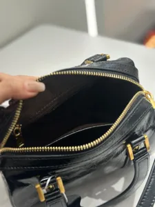Detailed view of black crinkled leather handbag interior, premium gold-tone hardware zipper.