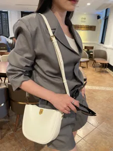 Detailed shot of stylish leather saddle bag worn by model in cafe, elegant shoulder strap.
