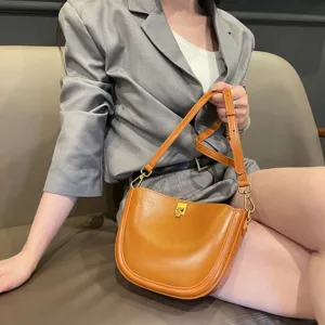 Close-up detail of stylish brown leather saddle bag with metal clasp and shoulder strap.