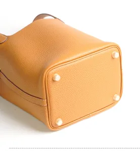 Genuine leather bucket bag detail view, premium yellow handbag with protective bottom studs.