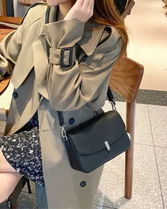 Detail shot of a sleek black leather crossbody bag paired with a classic trench coat in a cozy cafe.