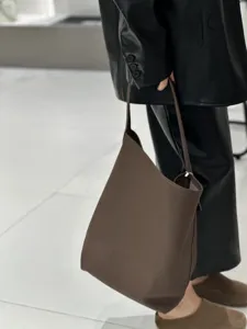 Dettaglio di borsa a secchiello in vera pelle marrone, stile minimalista spalla primo piano