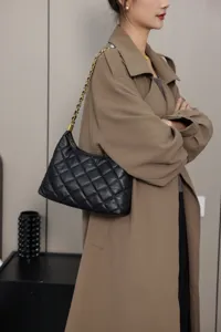 Detail shot of a stylish black quilted leather shoulder bag with a chic chain strap worn by a model.