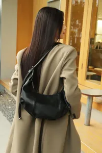 Close-up detail of the black leather pleated hobo underarm bag worn over shoulder outdoors.