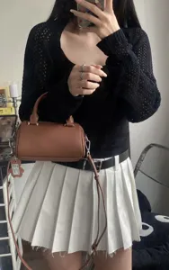 Close-up detail of brown leather Boston pillow handbag with contrast white stitching and strap.