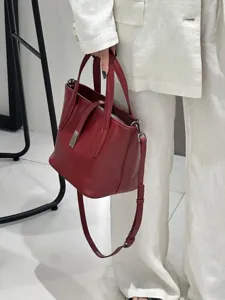 Dark red genuine leather bucket bag detail, elegant top-handle shoulder bag with metal clasp.