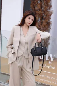 Detail shot of a sleek black leather Boston pillow handbag paired with a stylish beige suit.