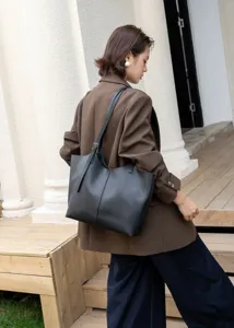 Detail view of a stylish black leather tote bag worn by a model outdoors in casual style.