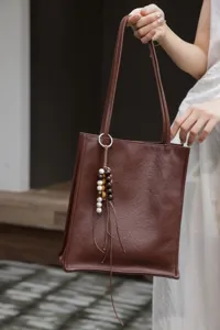 Brown leather tote bag detail view, showing soft genuine leather texture and wooden bead tassel.