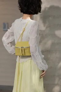 Detailed shot of a stylish yellow leather mini crossbody vanity box bag worn by a model.