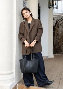 Outdoor lifestyle detail of black leather tote bag worn by model in brown blazer setting.