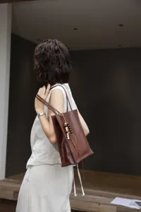 Detail shot of the dark brown leather tote bag with wooden bead pendant on shoulder.