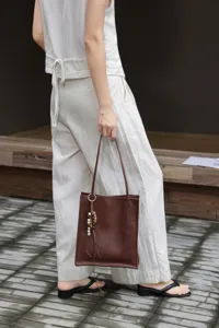Brown leather tote bag detail, featuring minimalist design, hanging beads, and shoulder strap.