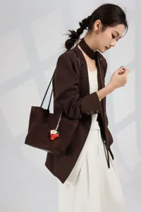 Detail view of the brown leather shoulder tote bag with cute strawberry charm and smooth texture.