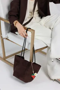 Brown suede shoulder tote bag detail shot with cute strawberry charm and slim black straps.