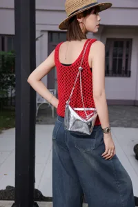Detailed shot of a stylish silver metallic shoulder bag worn outdoors with a chic red knit top.