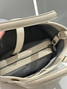 Detailed view of the premium leather handbag interior with striped lining and zipper pocket.