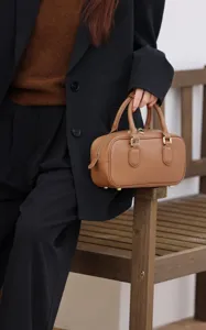 Detail shot of a classic brown boston bag pillow handbag with dual handles and gold tone hardware.