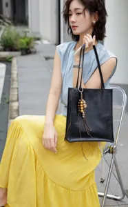 Close-up detail of black leather tote bag showing model styling in outdoor urban setting.