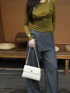 Detail shot of a minimalist white leather shoulder bag with a chic metal lock and slim strap.