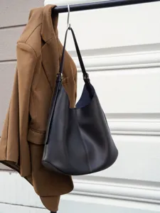 Detail view of black leather hobo shoulder bag hanging on wall, showing texture and hardware.